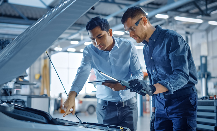 Shot of technician in training with supervisor looking under hood of car.
