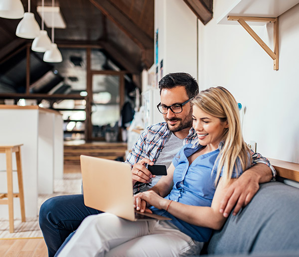 Couple shopping online while sitting on the sofa in modern apartment.
