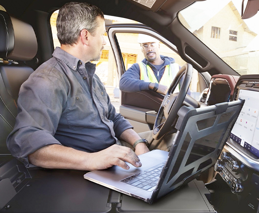A person in a parked 2022 Ford F-150 using his laptop