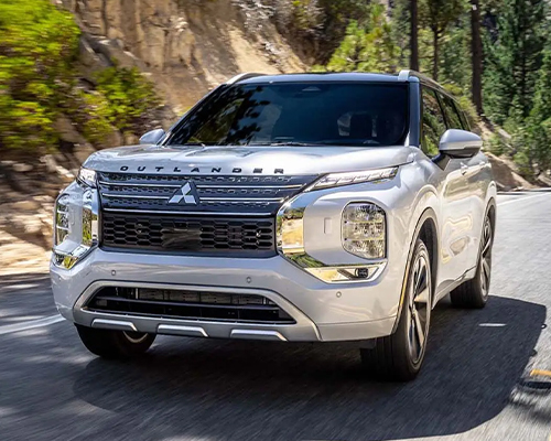 Front angled view of a white 2024 Outlander SUV driving on the road